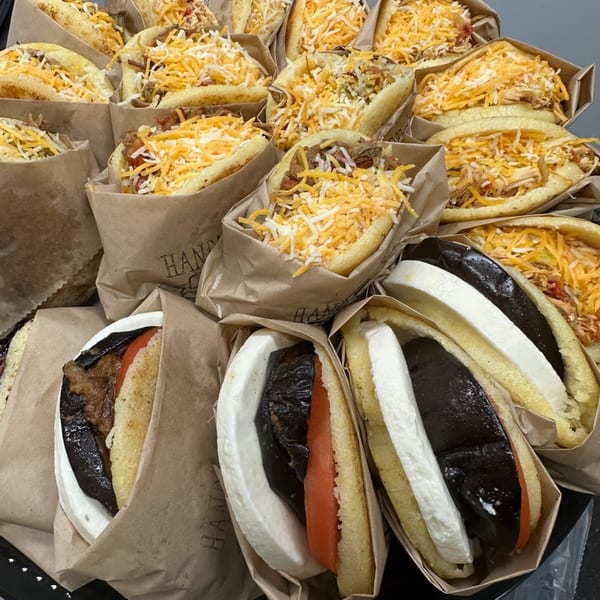 A tray of various arepas, some with shredded cheese, others with eggplant, tomato, and cheese.