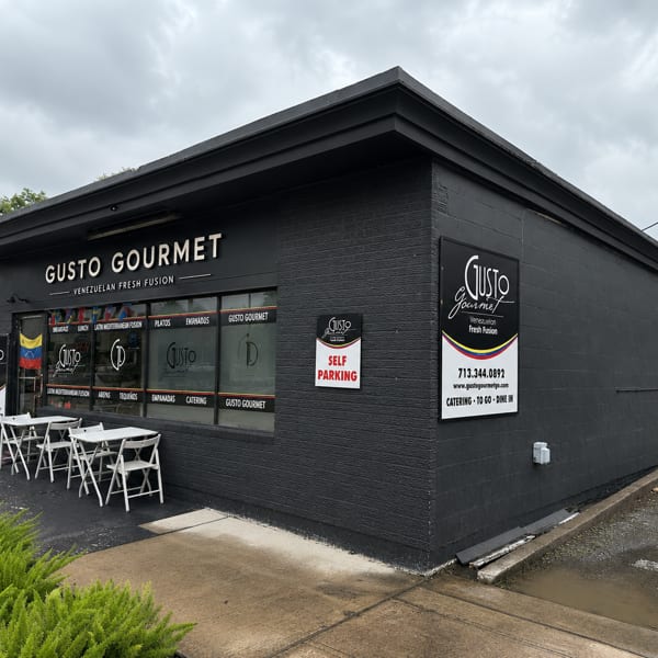 Exterior of Gusto Gourmet, a Venezuelan Fresh Fusion restaurant, with outdoor seating and dark gray facade.