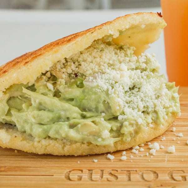 Arepa stuffed with creamy avocado chicken salad and crumbled white cheese on a wooden board.