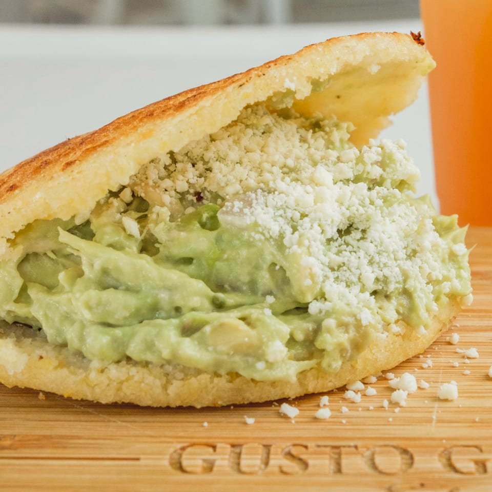 Arepa stuffed with creamy avocado chicken salad and crumbled white cheese on a wooden board.