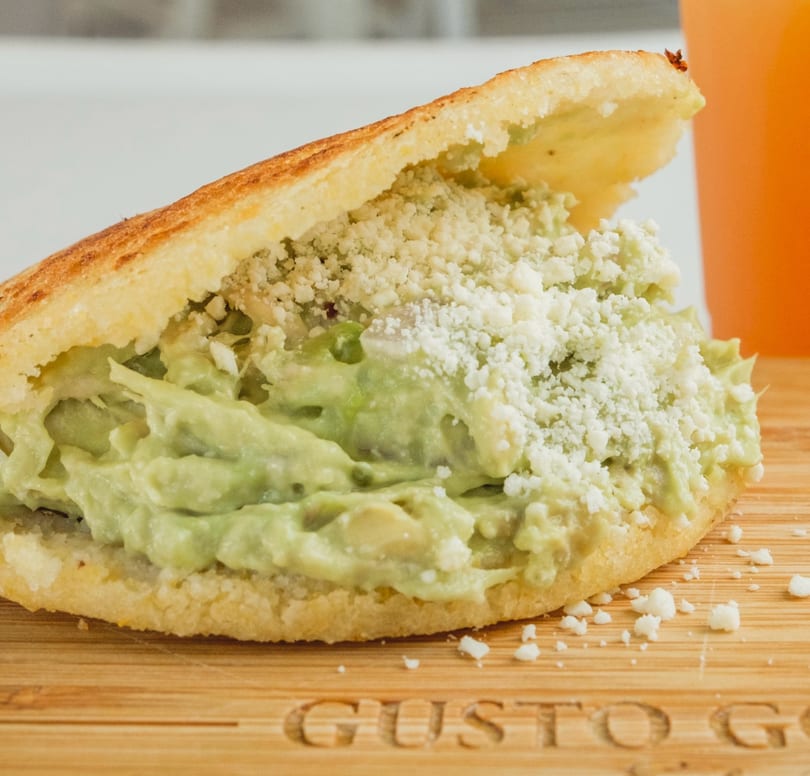 Arepa stuffed with creamy avocado chicken salad and crumbled white cheese on a wooden board.