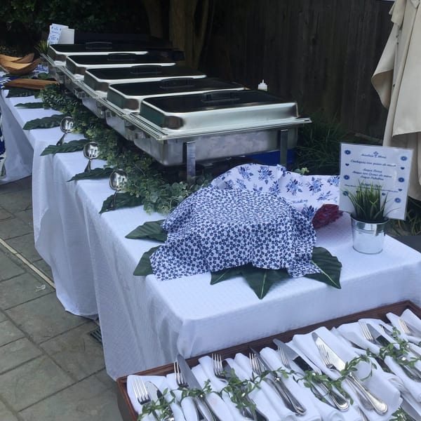 A buffet table with chafing dishes, blue and white patterned linens, and neatly arranged cutlery.