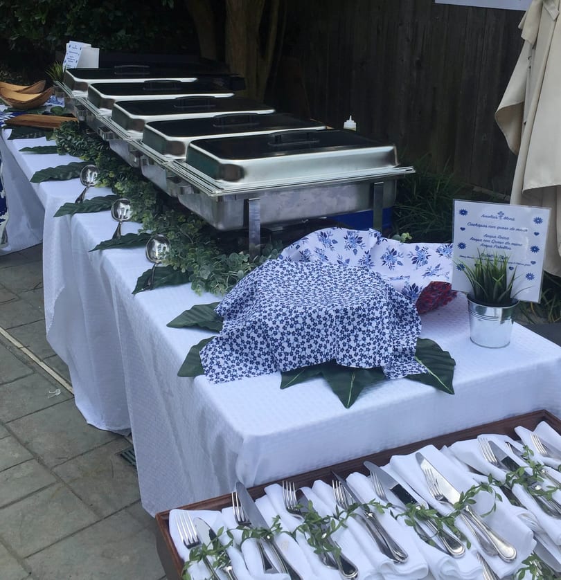A buffet table with chafing dishes, blue and white patterned linens, and neatly arranged cutlery.