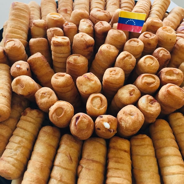 A platter of golden-brown Venezuelan tequeños, some with cheese and others with guava, and two Venezuelan flags.