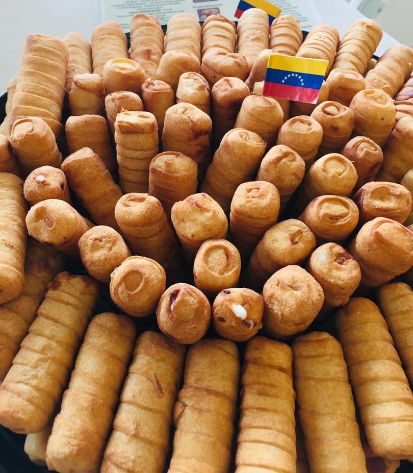 A platter of golden-brown Venezuelan tequeños, some with cheese and others with guava, and two Venezuelan flags.