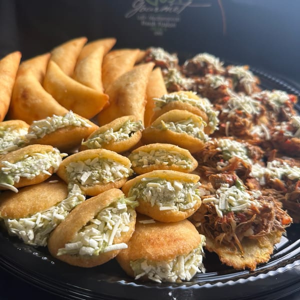 A platter of golden-brown empanadas, mini arepas with cheese and avocado, and shredded meat with cheese.